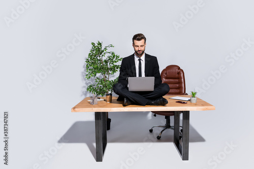Full body photo of handsome business guy hold notebook chatting colleagues good mood sitting table lotus yoga pose wear blazer shirt pants shoes suit isolated grey background © deagreez