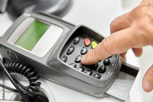 shopping, payment and finance concept - close up of hand with credit card in card-reader entering pin code