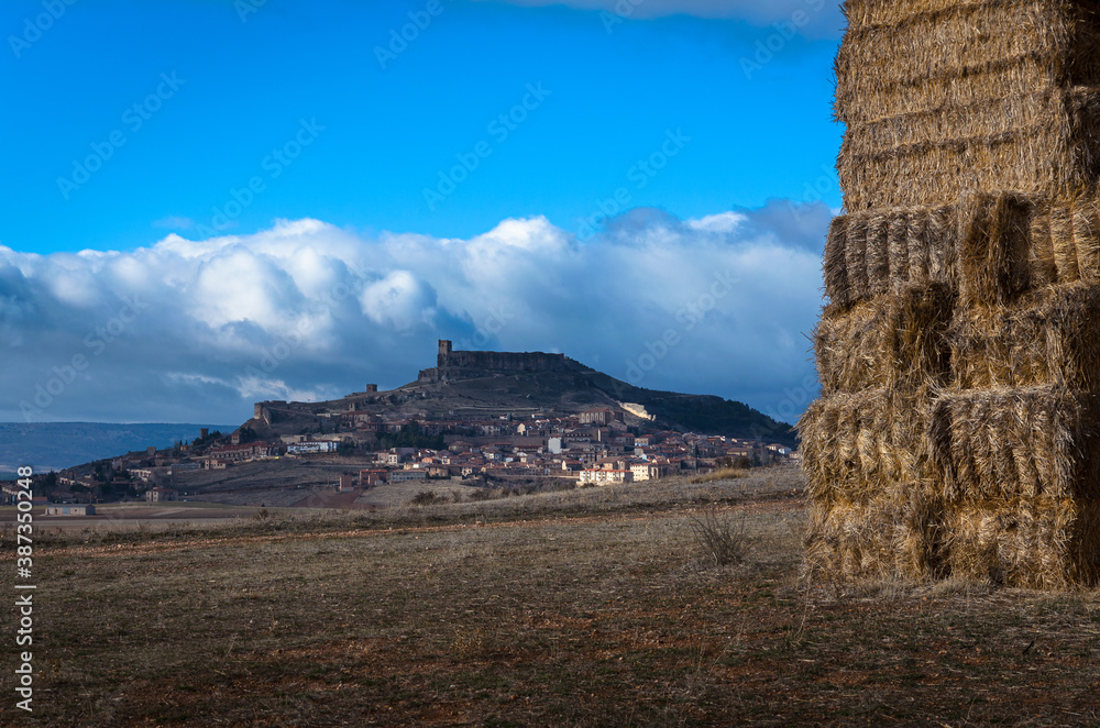 Landscape of the medieval city of Atienza with a cloudy blue sky and bundles of hay in a dry field, Guadalajara, Spain