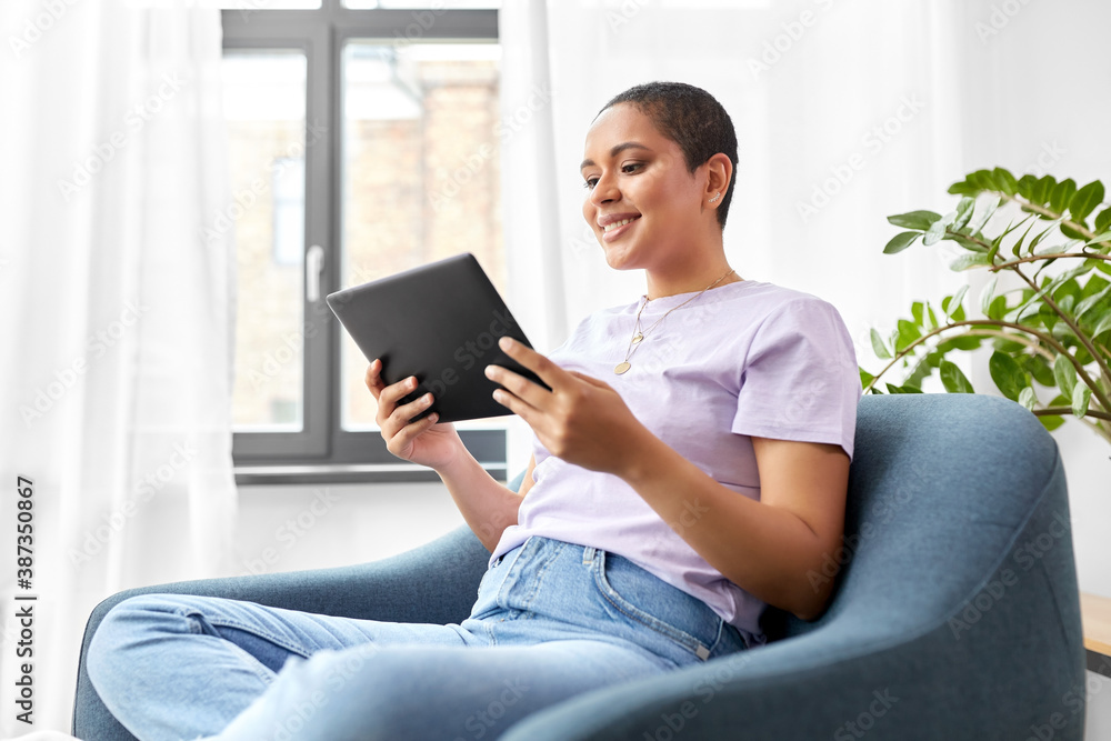 people, technology and leisure concept - happy young african american woman with tablet pc computer sitting in chair at home people, technology and leisure concept - happy young african american woman with tablet pc computer sitting in chair at home