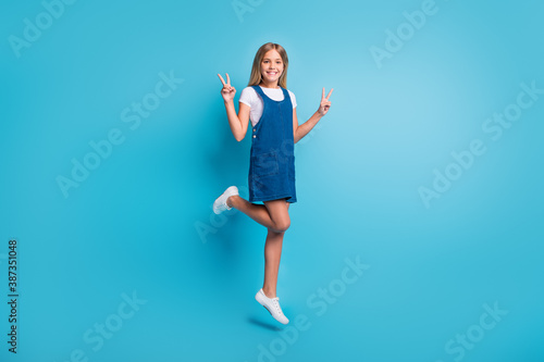 Full size photo of nice cool girl jumping show v-sign wear t-shirt dress shoes isolated on pastel blue color background