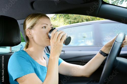 Frau fährt Auto und trinkt Kaffee oder Tee aus Thermobescher und ist dabei abgelenkt vom Verkehr auf der Straße © Dan Race
