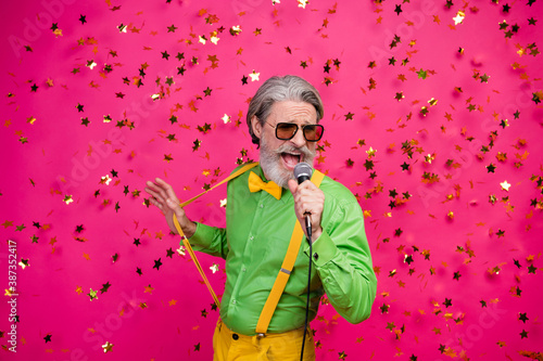Photo of funny aged grandpa club party singing karaoke microphone confetti fall excited singer wear sun specs green shirt yellow suspenders tie isolated shine pink color background