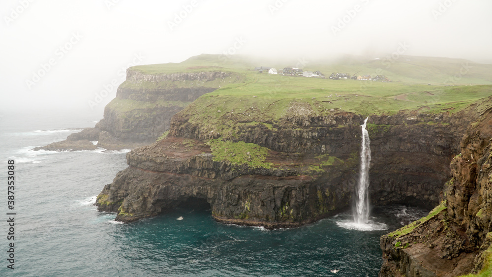 Múlafossur Waterfall in Gásadalur village on a misty day in bad weather on the Faroe Islands in Denmark. Múlafossur Waterfall in Gásadalur village on a misty day in bad weather on the Faroe Islands in Denmark.