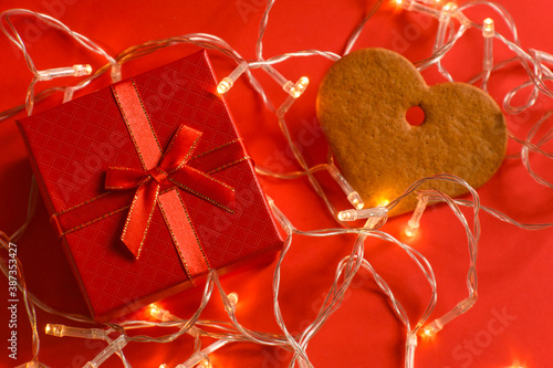 gift box and heart shaped gingerbread cookies on a red background with garlands. christmas, new year, valentine's day. selective focus