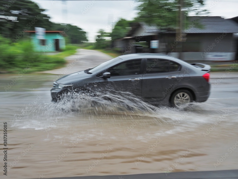 A black car is running on a road with water on the road. A black car is running on a road with water on the road.