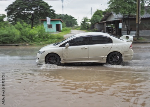 A white car is running on a road with water on the road. © กุลชาญ   สุขสมถิ่น