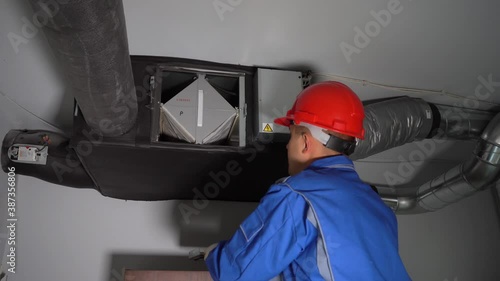 Technician man with helmet checking air ventilation recuperator system filters