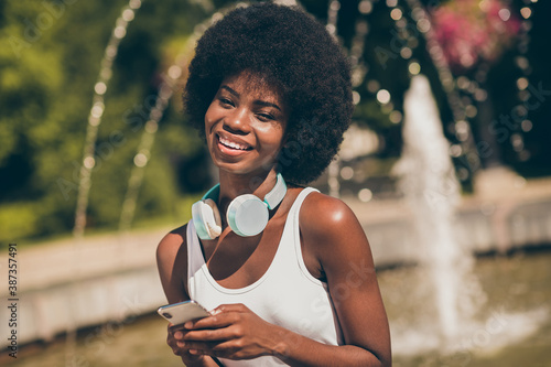 Portrait of positive cheerful afro american girl hold smartphone in summer spring fountain town center park