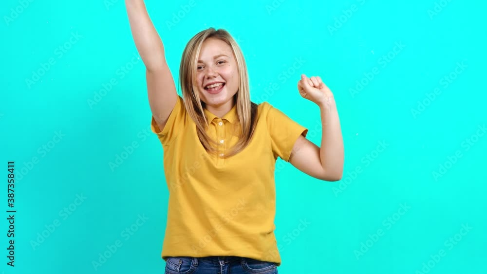 The modest young woman making the winning gesture, says Yes, gestures expressively with her hands. Beautiful Caucasian woman in yellow T-shirt and long blond hair standing on blue background. A little The modest young woman making the winning gesture, says Yes, gestures expressively with her hands. Beautiful Caucasian woman in yellow T-shirt and long blond hair standing on blue background. A little