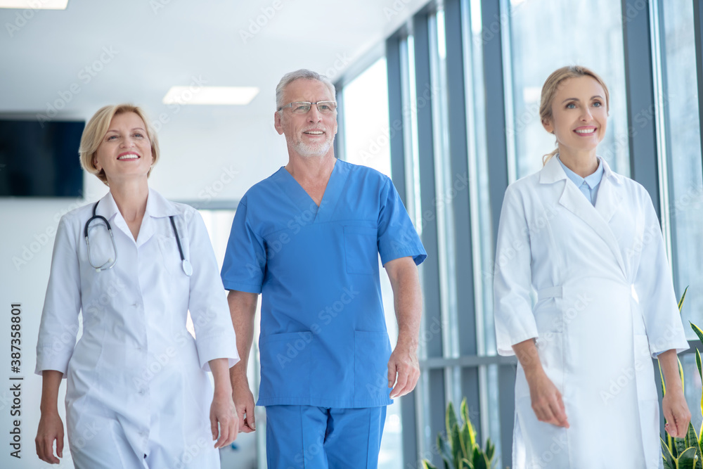 Group of smiling medical workers walking along hospital hallway Group of smiling medical workers walking along hospital hallway