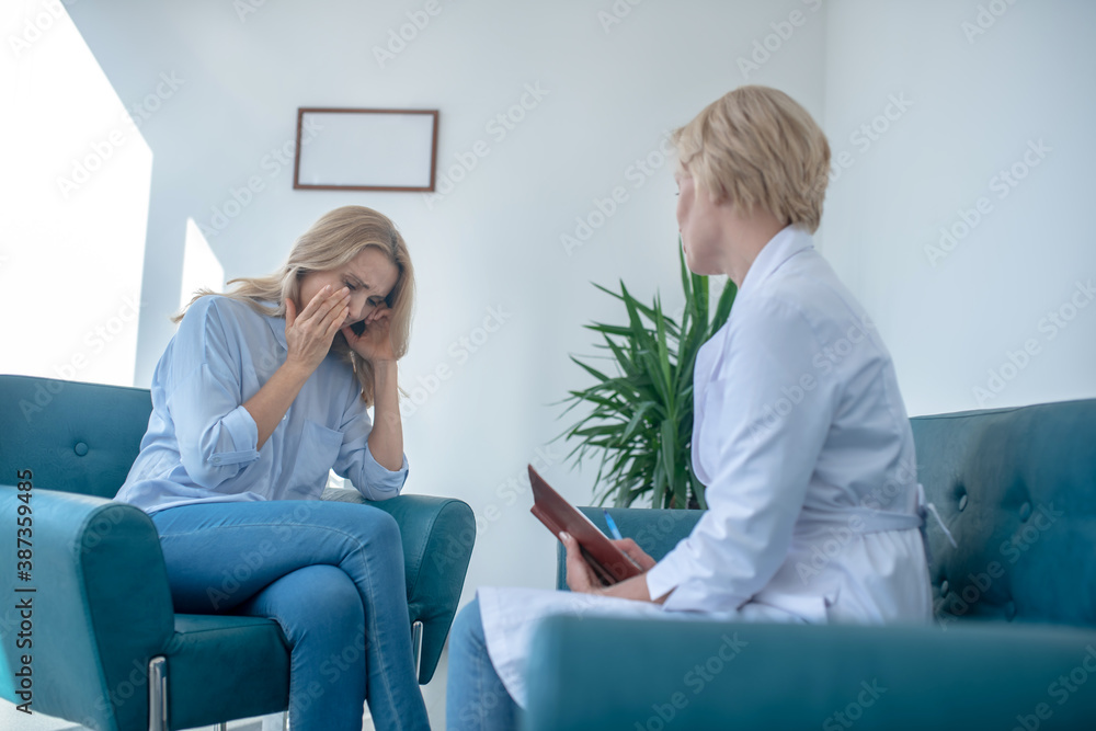 Desperate female patient crying, sitting opposite mature blonde female doctor Desperate female patient crying, sitting opposite mature blonde female doctor