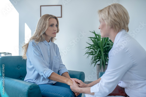 Photography Blonde female doctor soothing female patient, holding her hands