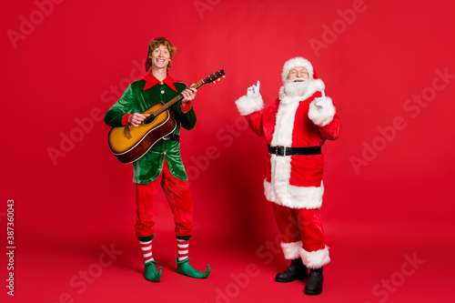 Photo of two people elf play guitar santa enjoy wear x-mas costume coat headwear isolated red color background