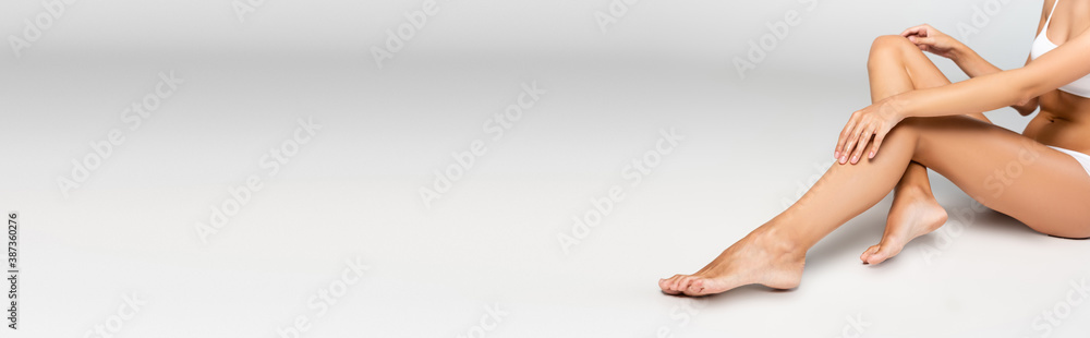 Woman holding hands on knee, while sitting with smooth legs on grey, banner Woman holding hands on knee, while sitting with smooth legs on grey, banner