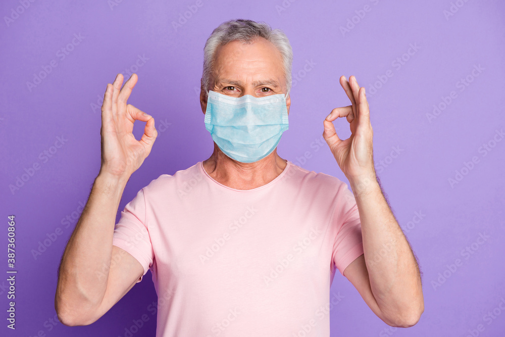 Photo of retired old man raise two hands show okey wear blue face mask isolated violet color background Photo of retired old man raise two hands show okey wear blue face mask isolated violet color background