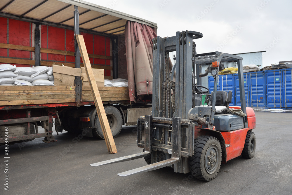 Red forklift stands next to a truck trailer
