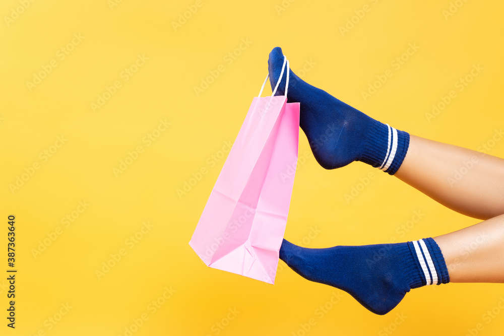 Φωτογραφία Cropped view of pink paper bag hanging on woman leg in socks isolated on yellow