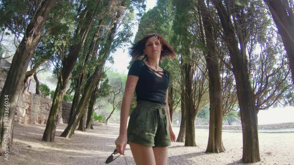 Back view of young charming woman walking away through green alley along pines at the sunset. Back view of young charming woman walking away through green alley along pines at the sunset.