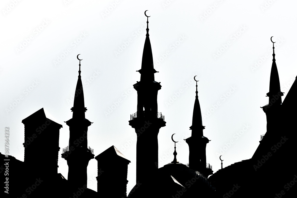 Black silhouette of a Muslim mosque against a bright sky. Towers of the mosque with a Crescent.