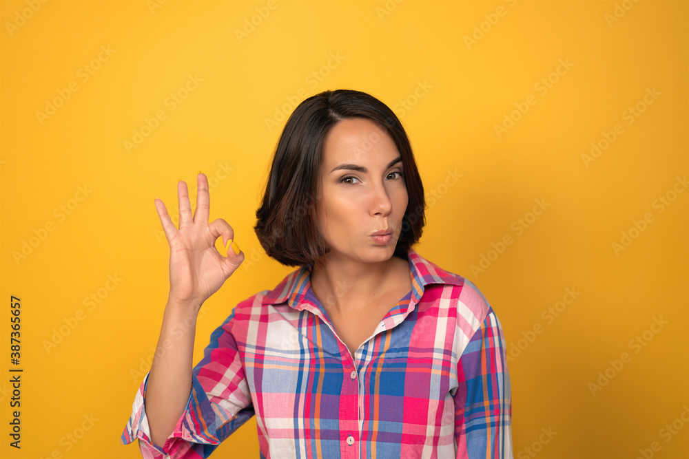Young pretty woman shows okey sign. Isolated on yellow wall at background. Copy space. Young pretty woman shows okey sign. Isolated on yellow wall at background. Copy space.