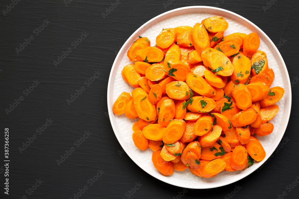 Homemade Sauteed Carrots on a plate on a black surface, top view. Flat lay, overhead, from above. Space for text. Homemade Sauteed Carrots on a plate on a black surface, top view. Flat lay, overhead, from above. Space for text.