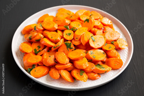 Homemade Sauteed Carrots on a plate on a black background, low angle view.