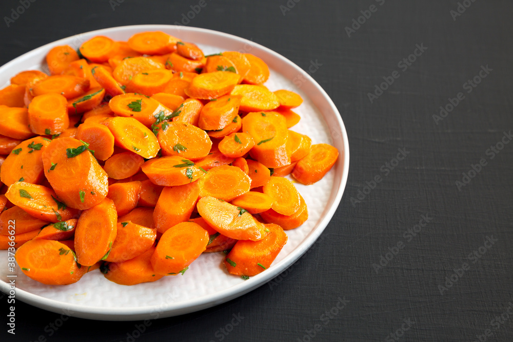 Homemade Sauteed Carrots on a plate on a black background, side view. Copy space. Homemade Sauteed Carrots on a plate on a black background, side view. Copy space.