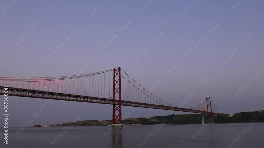 Evening to night time lapse shot of 25th of April Bridge at Lisbon. Car traffic congestion seen on road, peak hour at end of work day. Scenic shot of Portugal capital city landmark Evening to night time lapse shot of 25th of April Bridge at Lisbon. Car traffic congestion seen on road, peak hour at end of work day. Scenic shot of Portugal capital city landmark