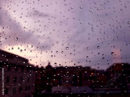 Genova, Italy - 10/22/2020: Water​ rain​ drops​ on​ glass​ background.​ Rain​ drops​ on​ a​ Windows. Hdden sunset in autumn after rain.