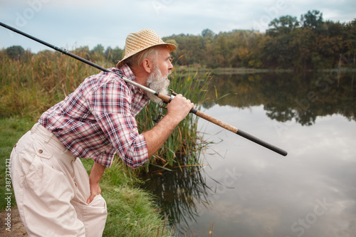 Elderly bearded man looking away at the lake, holding his fishing rod
