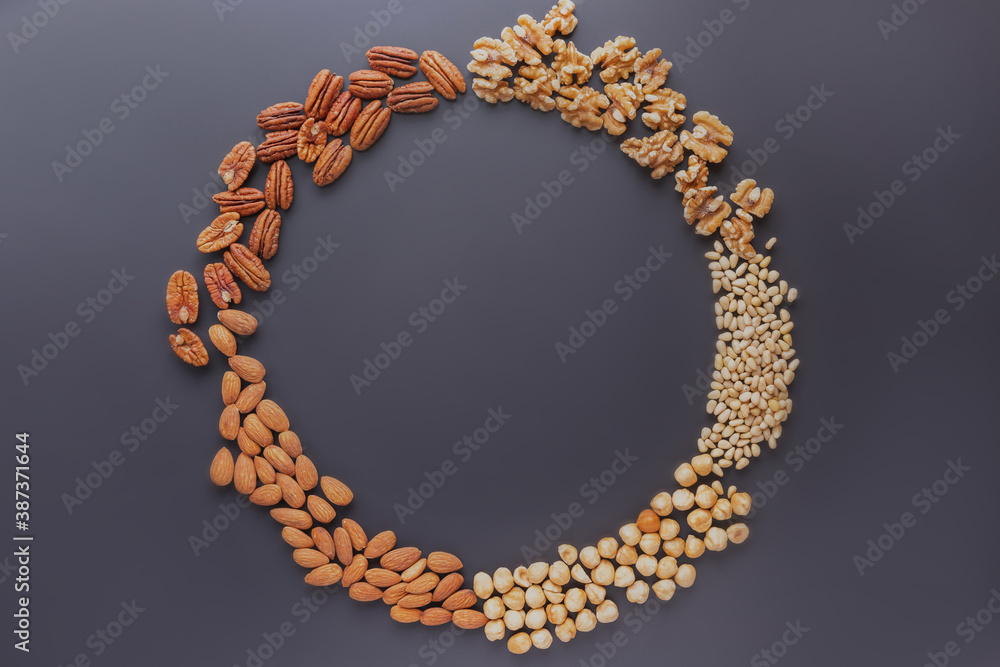 almond, pine, pecan nuts, walnuts, hazelnuts forming a round frame on a grey table almond, pine, pecan nuts, walnuts, hazelnuts forming a round frame on a grey table