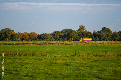 a bright yellow truck  drives on a distant country road through the idyll