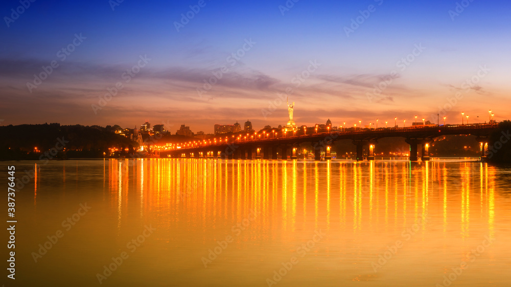 Amazing cityscape of Kyiv (Kiev) in national colors - blue and yellow, scenic panoramic view of the Paton bridge, Motherland monument and Dnieper river at dusk with city lights, capital of Ukraine