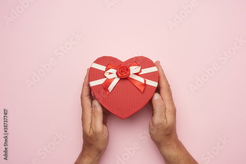 male hand holding a red cardboard box with a bow on a pink background