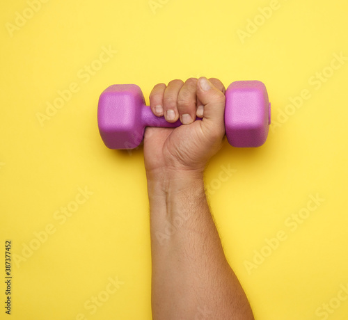 male hand holds a purple one kilogram dumbbell
