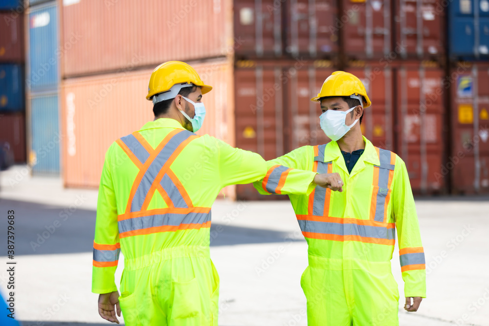 New normal greeting in the office to be safe from the coronavirus. Mask protection against virus. Covid-19, coronavirus pandemic. Man worker in hardhat helmet at container yard New normal greeting in the office to be safe from the coronavirus. Mask protection against virus. Covid-19, coronavirus pandemic. Man worker in hardhat helmet at container yard