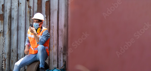 Man worker wearing protection face mask during coronavirus and flu outbreak and safety hardhat helmet at container yard. Import and Export concept.