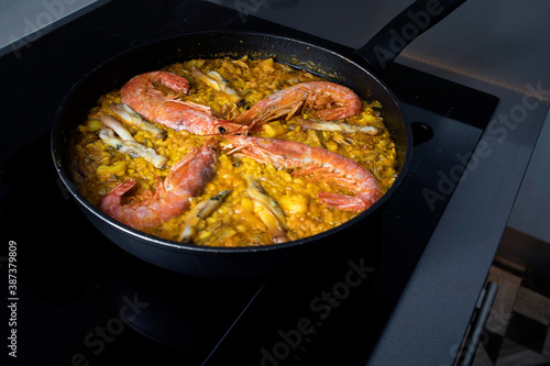Traditional spanish seafood paella in the fry pan on a black cooker.