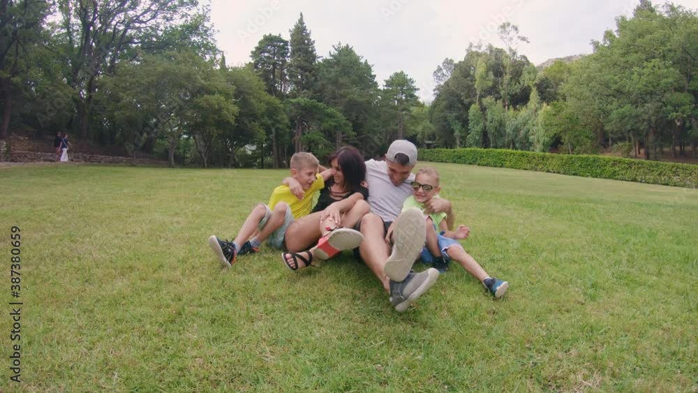 Two boys running to their parents and hugging them, when mom and dad sitting on the grass in park and enjoying a warm sunny day. Two boys running to their parents and hugging them, when mom and dad sitting on the grass in park and enjoying a warm sunny day.