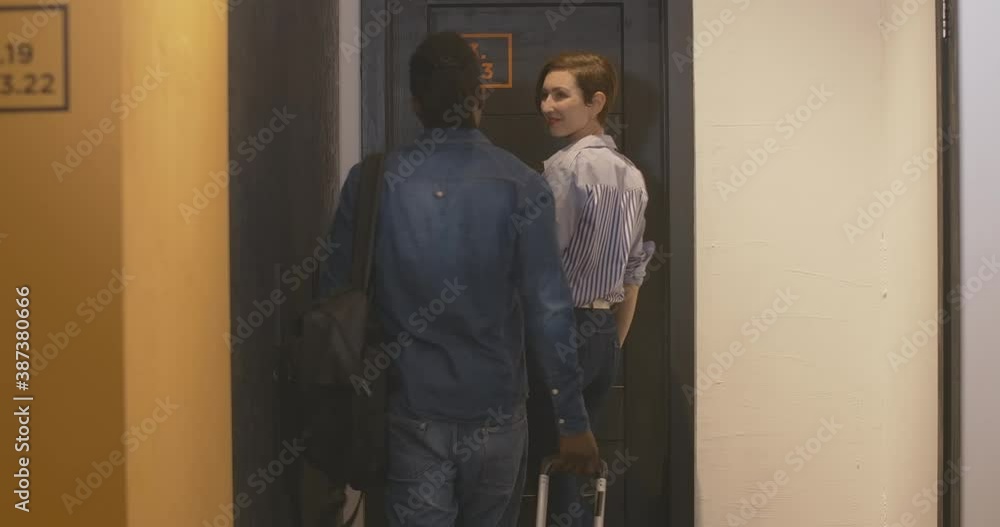 Young interracial couple entering room in hostel or hotel and closing door. Charming Caucasian woman and handsome African American man with travel bag checking in. Tourists travelling together. Young interracial couple entering room in hostel or hotel and closing door. Charming Caucasian woman and handsome African American man with travel bag checking in. Tourists travelling together.