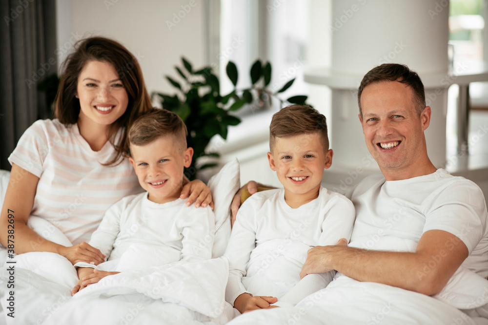 Young family enjoying in bed. Happy parents with sons relaxing in bed.. Young family enjoying in bed. Happy parents with sons relaxing in bed..