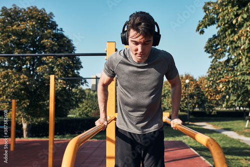Obraz na plátně Young man doing dips on parallel bars during his workout in a modern calisthenics street workout park