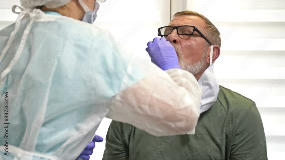 Lab technician in a protective suit takes a swab from an elderly patient for coronavirus. Lab technician in a protective suit takes a swab from an elderly patient for coronavirus.