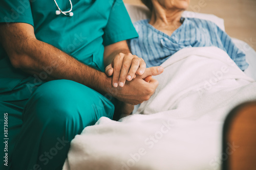 Close up of male doctor hands holding senior woman patient hand in hospital bed. comforting and support patient.