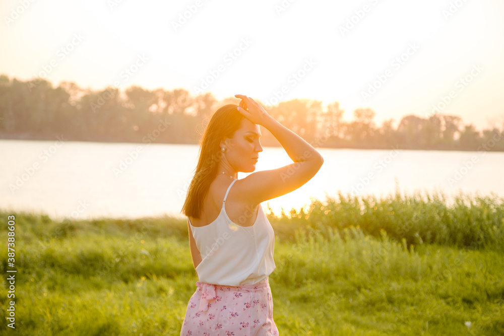 Gentle silhouette of a girl in the rays of the setting sun on the river bank.