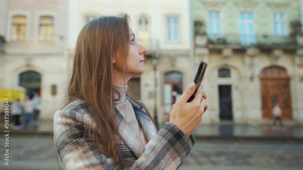 Woman walking down an old street and using smartphone, taking photos of buildings around Woman walking down an old street and using smartphone, taking photos of buildings around