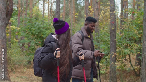 Wallpaper Mural Side view of cheerful lovely multiethnic travelers couple on hike walking through beautiful autumn woodland with trekking poles and backpacks, exploring wild nature, enjoying active healthy lifestyle. Torontodigital.ca