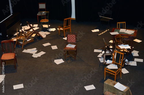 Old-fashioned chairs, chests and pieces of paper put in a mess on a theatre stage photo