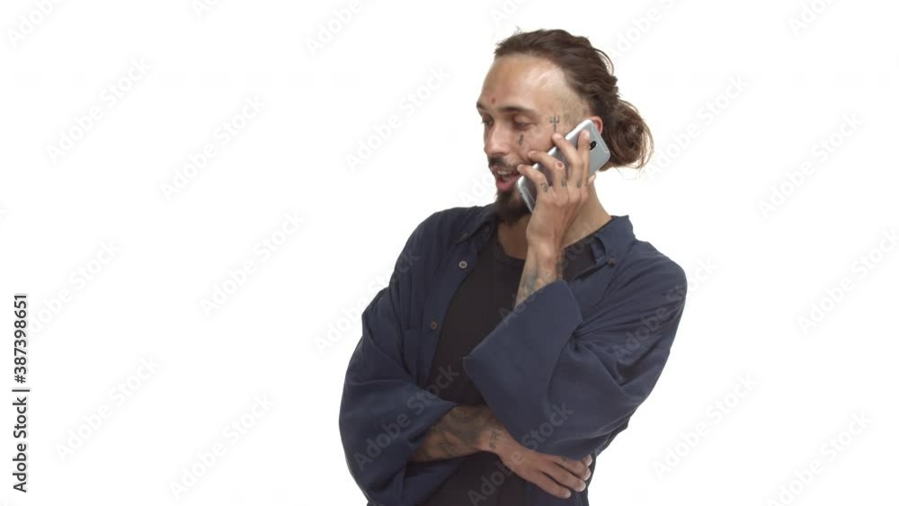 Handsome hipster with beard and tattooed face, talking on mobile phone, nodding and agreeing during conversation, standing over white background Handsome hipster with beard and tattooed face, talking on mobile phone, nodding and agreeing during conversation, standing over white background